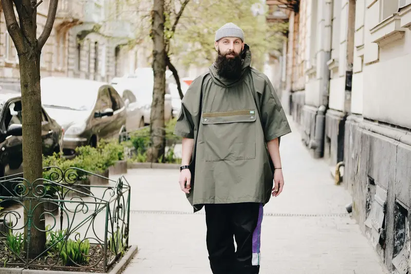 Bearded man walking in an urban street wearing a khaki poncho with hood and front pocket